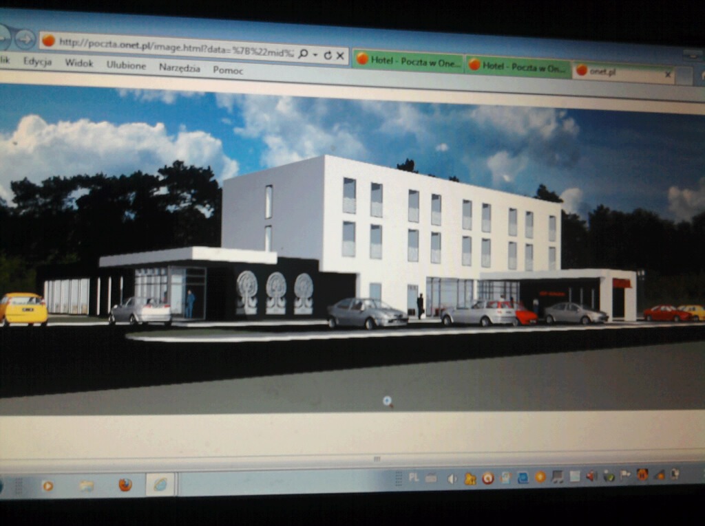 Wizualizacja architektoniczna nowoczesnego, trzypiętrowego budynku usługowego z płaskim dachem i rzędem zaparkowanych samochodów przed wejściem, wyświetlana na ekranie komputera.