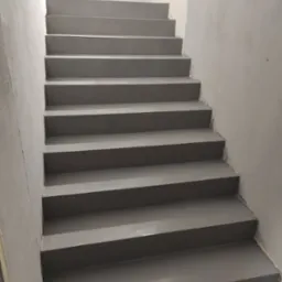 Szare schody wewnątrz budynku, wykończone gładką powierzchnią, prawdopodobnie z użyciem specjalistycznej powłoki. Widoczne niedoskonałości wykończenia przy ścianach.