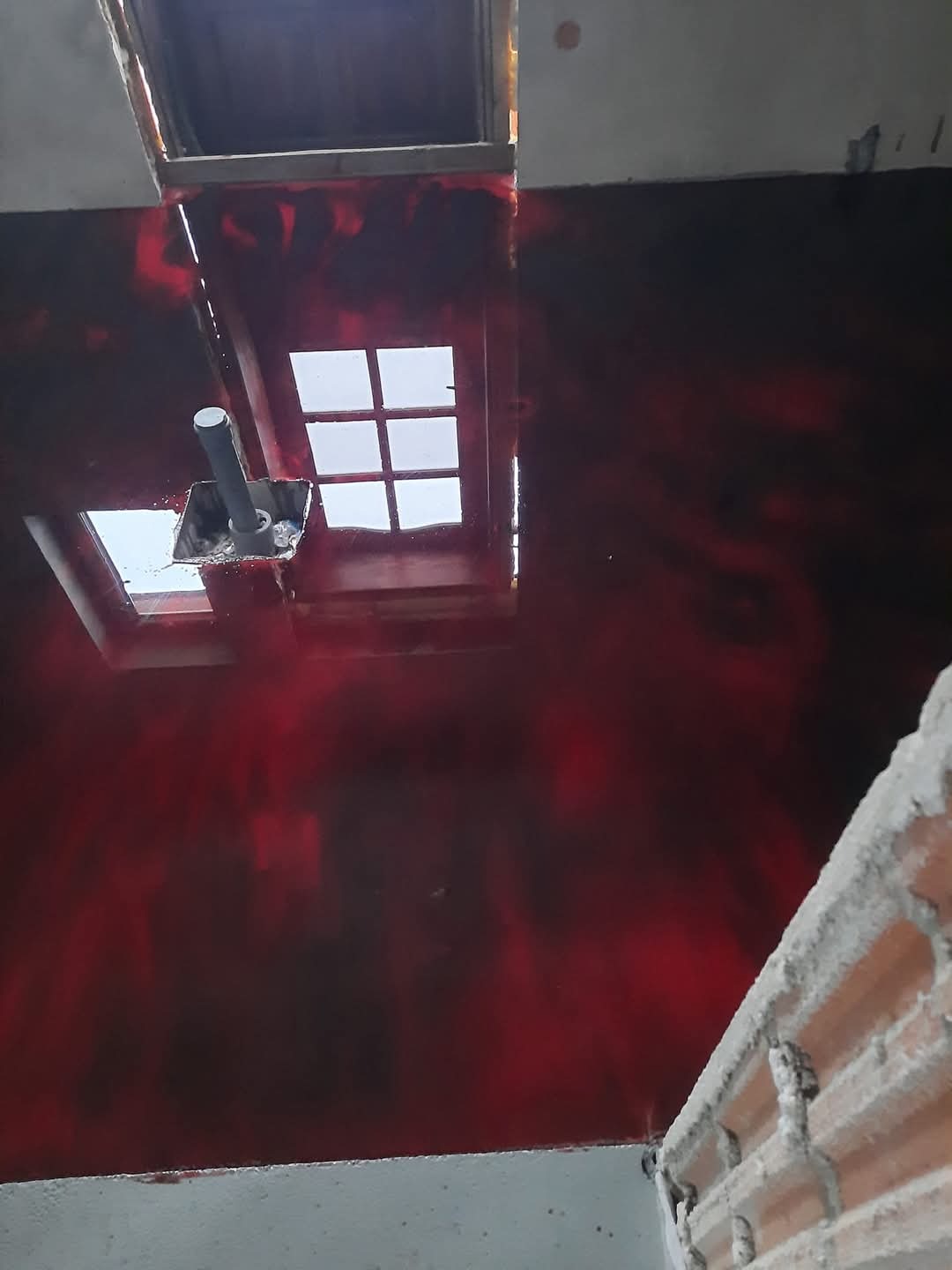 Czerwona, wzorzysta posadzka w trakcie aplikacji. Widoczne okna dachowe i fragment ściany z cegły. Charakterystyczny wzór na powierzchni.