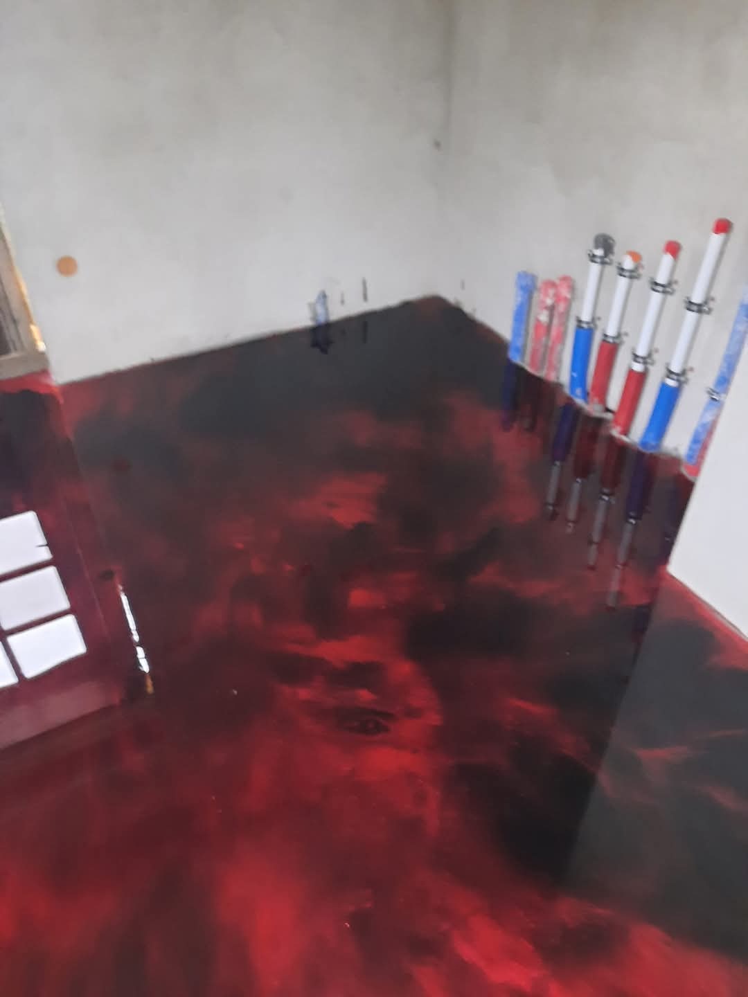 Błyszcząca, czerwono-czarna posadzka żywiczna z widocznymi rurami grzewczymi przy ścianie. Nietypowy wzór i połysk nadają wnętrzu nowoczesny charakter.