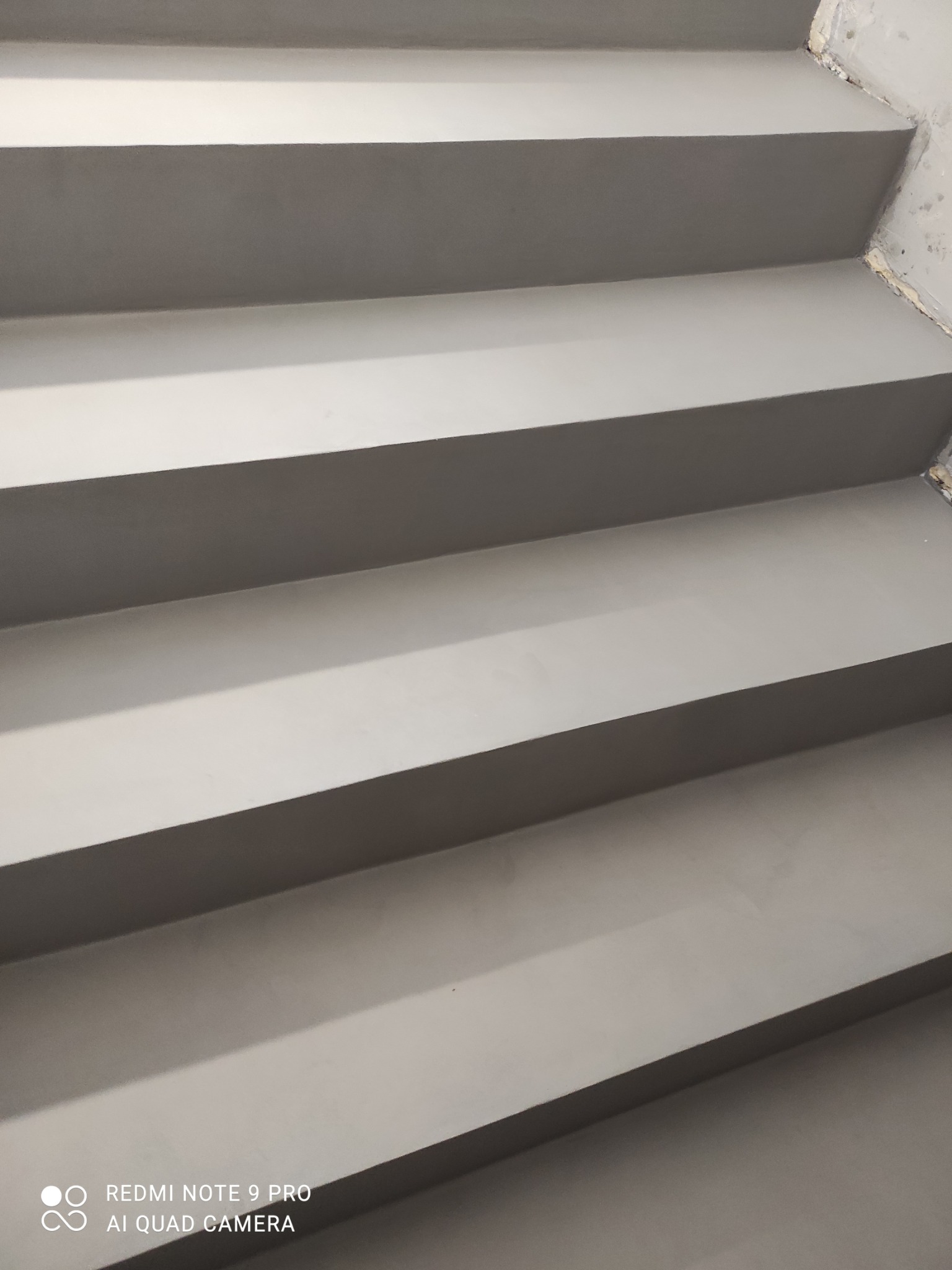 Szare schody pokryte jednolitą, gładką powierzchnią, prawdopodobnie wykonane z materiału imitującego beton. Widok z góry na kilka stopni schodów.