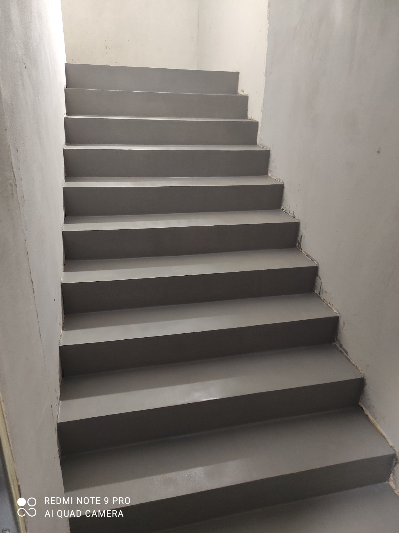 Szare schody wewnątrz budynku, wykończone gładką powierzchnią, prawdopodobnie z użyciem specjalistycznej powłoki. Widoczne niedoskonałości wykończenia przy ścianach.