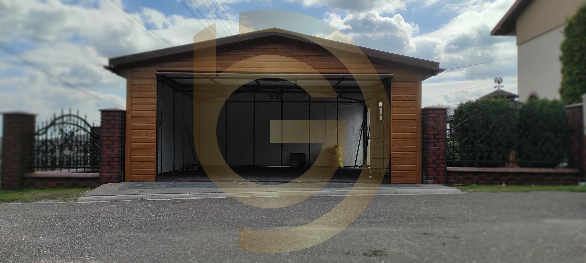 Drewniany garaż z otwartą bramą segmentową, widoczny z zewnątrz na tle pochmurnego nieba i domu z ogrodem