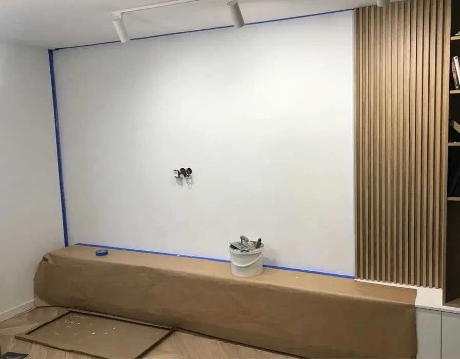 Przygotowana ściana do malowania z zabezpieczonymi elementami, widoczne listwy dekoracyjne, puszka z narzędziami i taśma malarska.