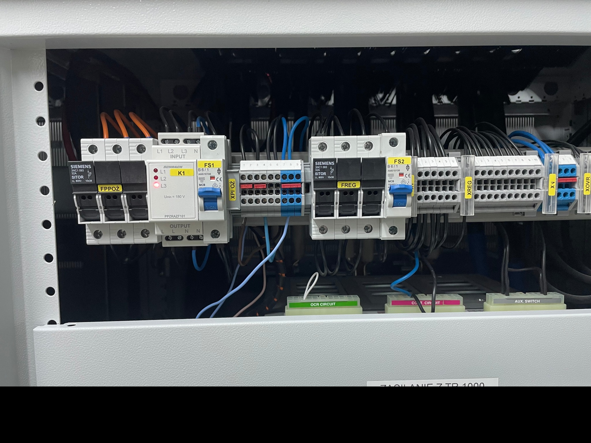 Rozdzielnica elektryczna wewnątrz szafy sterowniczej. Widoczne bezpieczniki, styczniki, przewody i listwy zaciskowe. Elementy oznaczone etykietami.