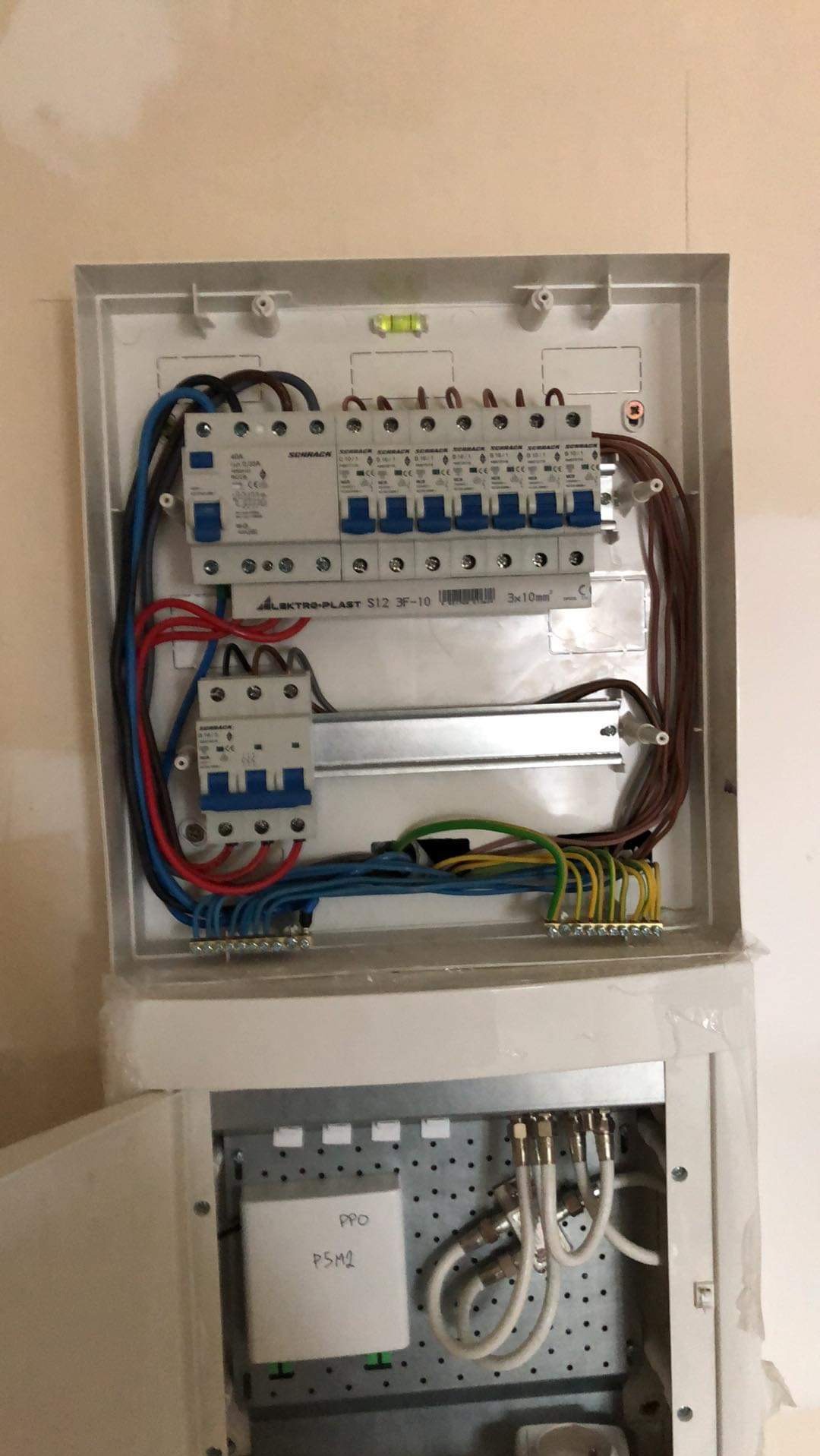 Rozdzielnia elektryczna w obudowie, widoczne zabezpieczenia, przewody i listwy zaciskowe. U góry poziomica. Na dole elementy instalacji antenowej.