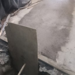 Grzegorz sitek - Wyrównywanie podłoża pod posadzkę przemysłową w Kołobrzegu, widoczny fragment wylanej masy, szpachla i wiadro w wykopie.