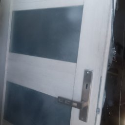 Grzegorz sitek - Białe drzwi wewnętrzne z poziomymi, szarymi szybami i nowoczesną, prostokątną klamką z metalu.