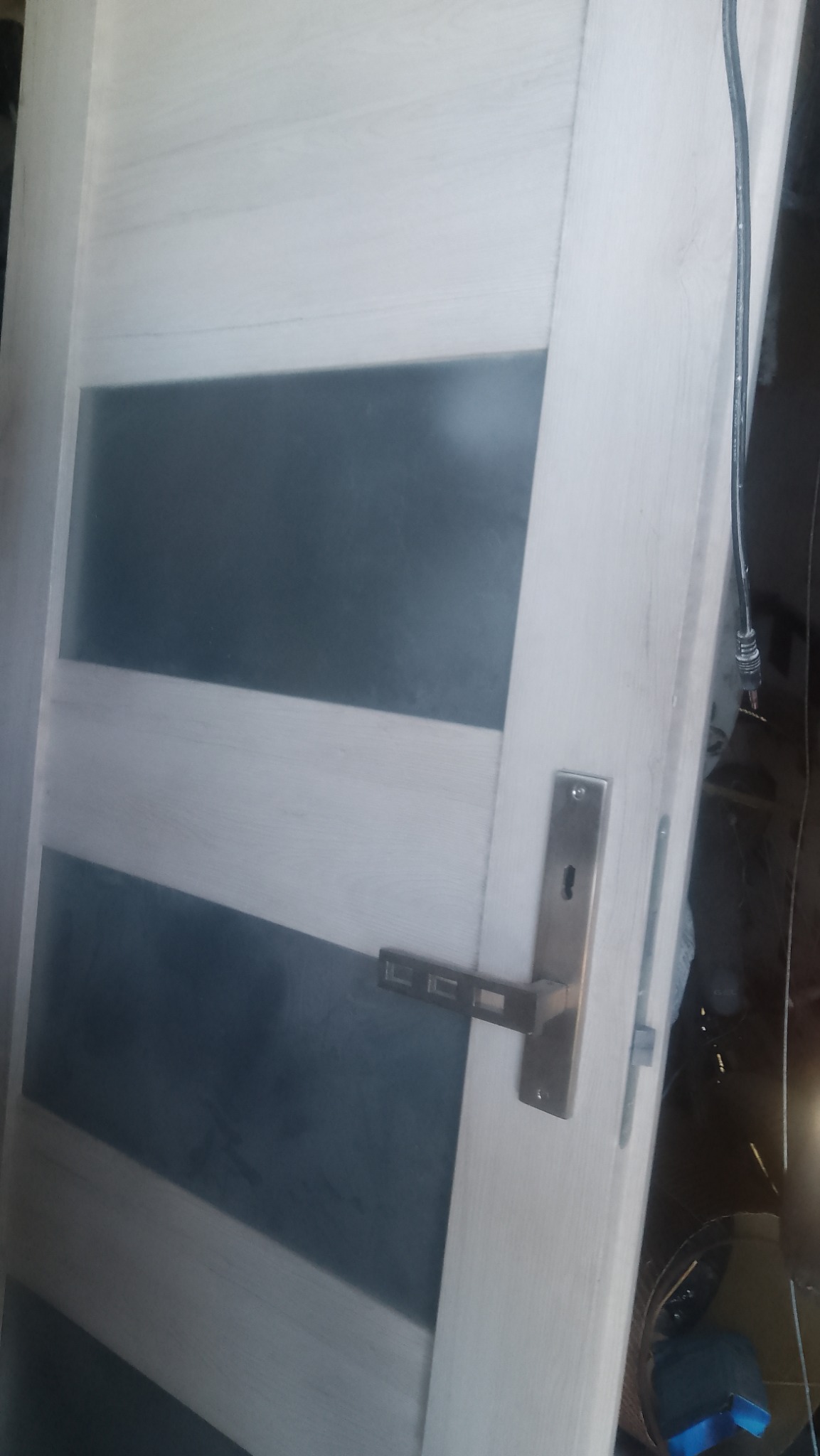 Białe drzwi wewnętrzne z poziomymi, szarymi szybami i nowoczesną, prostokątną klamką z metalu.