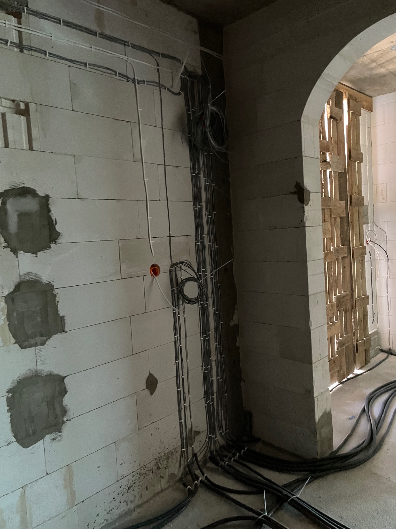 Surowy stan: kable elektryczne prowadzone po ścianie z betonu komórkowego, widoczne puszki instalacyjne i przewody ułożone wzdłuż ściany. W tle surowe przejście.