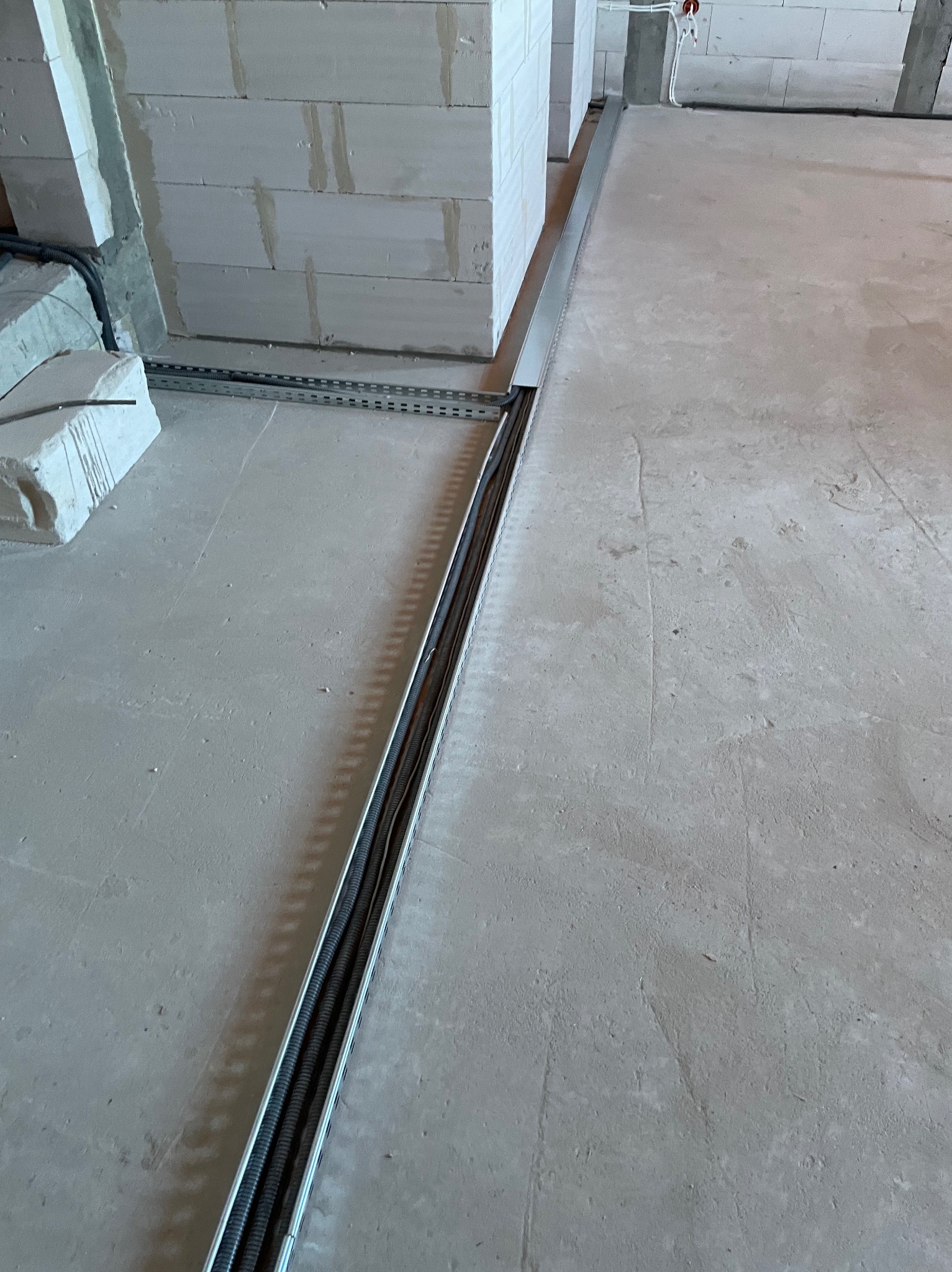 Instalacja elektryczna pod podłogą w korycie kablowym, widoczne przewody w peszlach, surowy stan, ściany z betonu komórkowego.