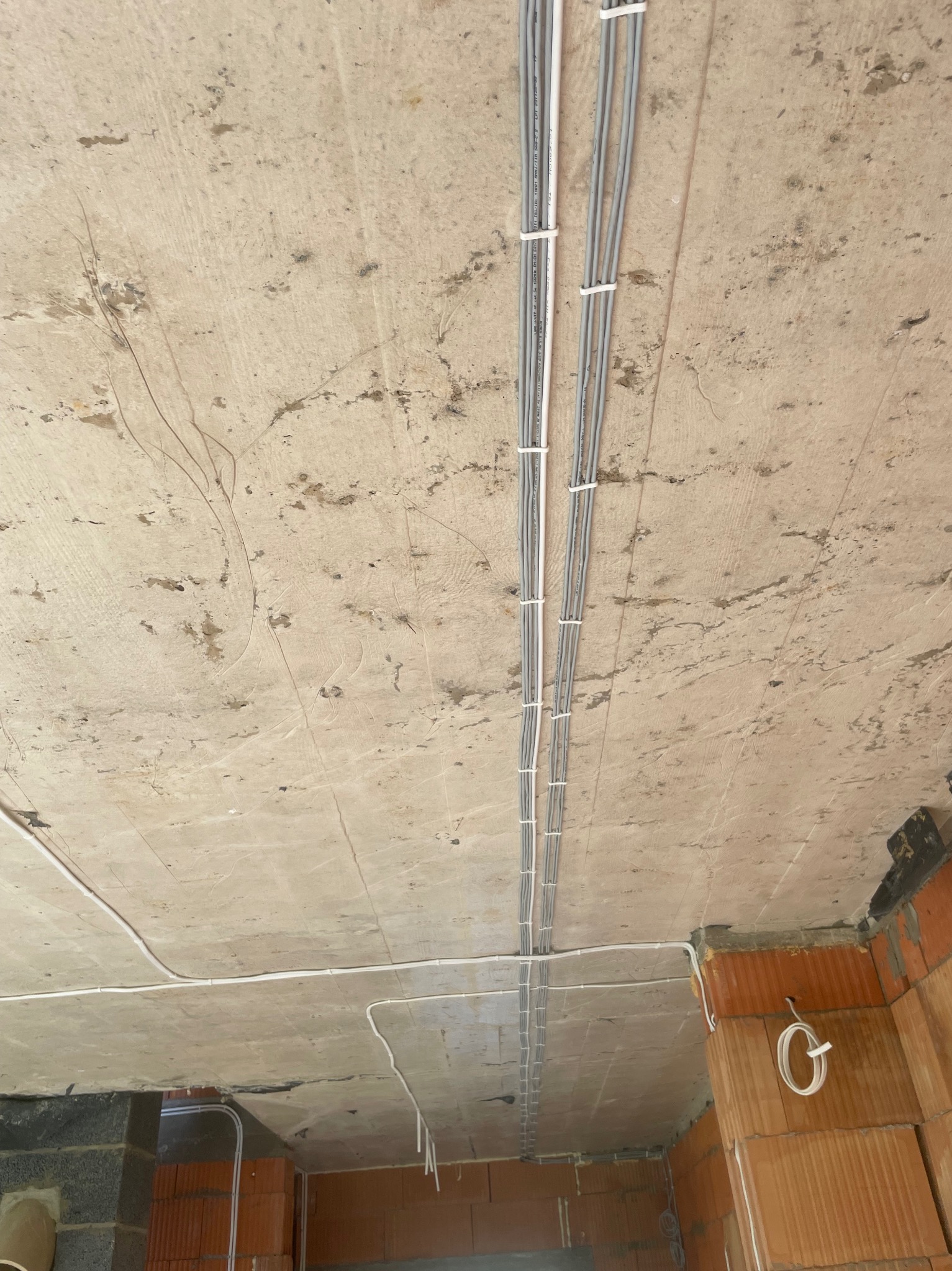 Szare kable elektryczne przymocowane do surowego betonowego sufitu w nowym budynku z ceglanymi ścianami. Widoczne przewody w peszlu.
