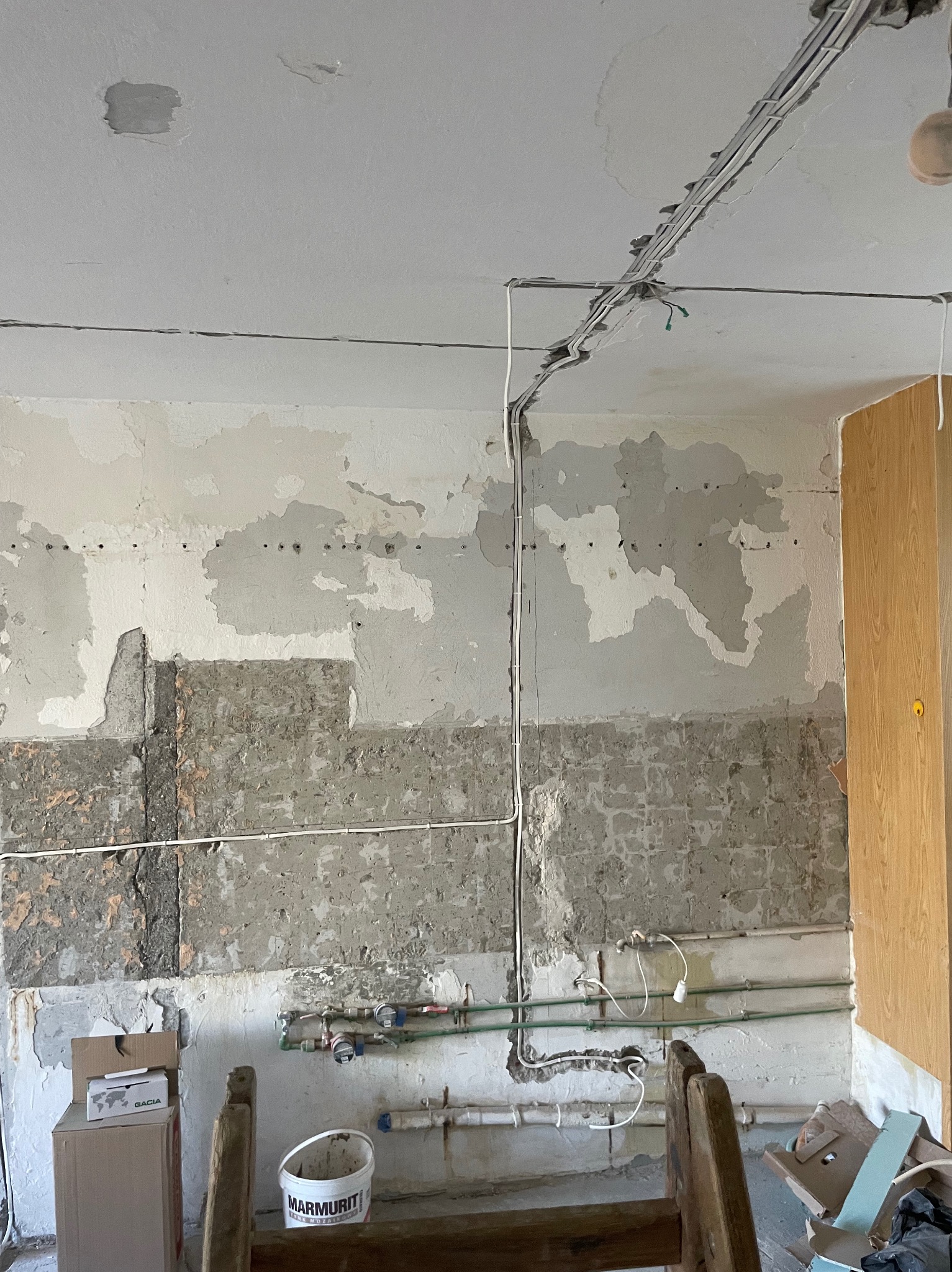 Remont kuchni w trakcie: ściany z odsłoniętym murem, widoczne przewody elektryczne pod sufitem i rury wodne. Fragment szafki kuchennej po prawej stronie.