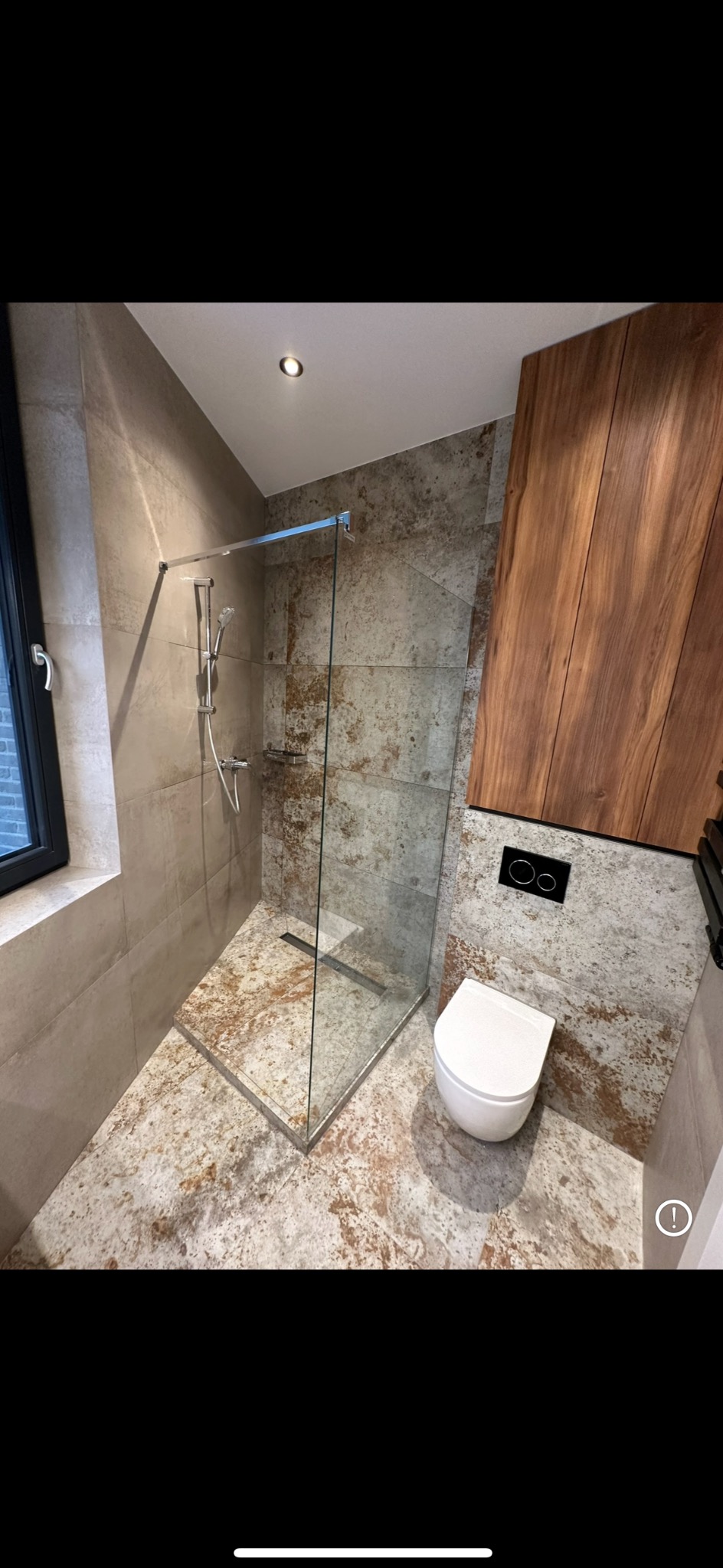 Nowoczesna łazienka w Warszawie z kabiną prysznicową typu walk-in z odpływem liniowym, płytkami imitującymi kamień na ścianach i podłodze oraz drewnianą zabudową nad toaletą w kolorze orzecha.