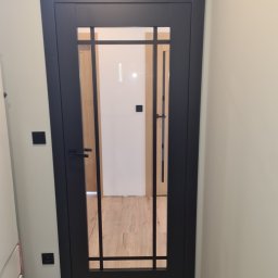 MPSMONT PIOTR KOZAKIEWICZ - Czarne, przeszklone drzwi wewnętrzne z klamką, zamontowane w mieszkaniu w Rudzie Śląskiej. Widoczny fragment podłogi i ściany.