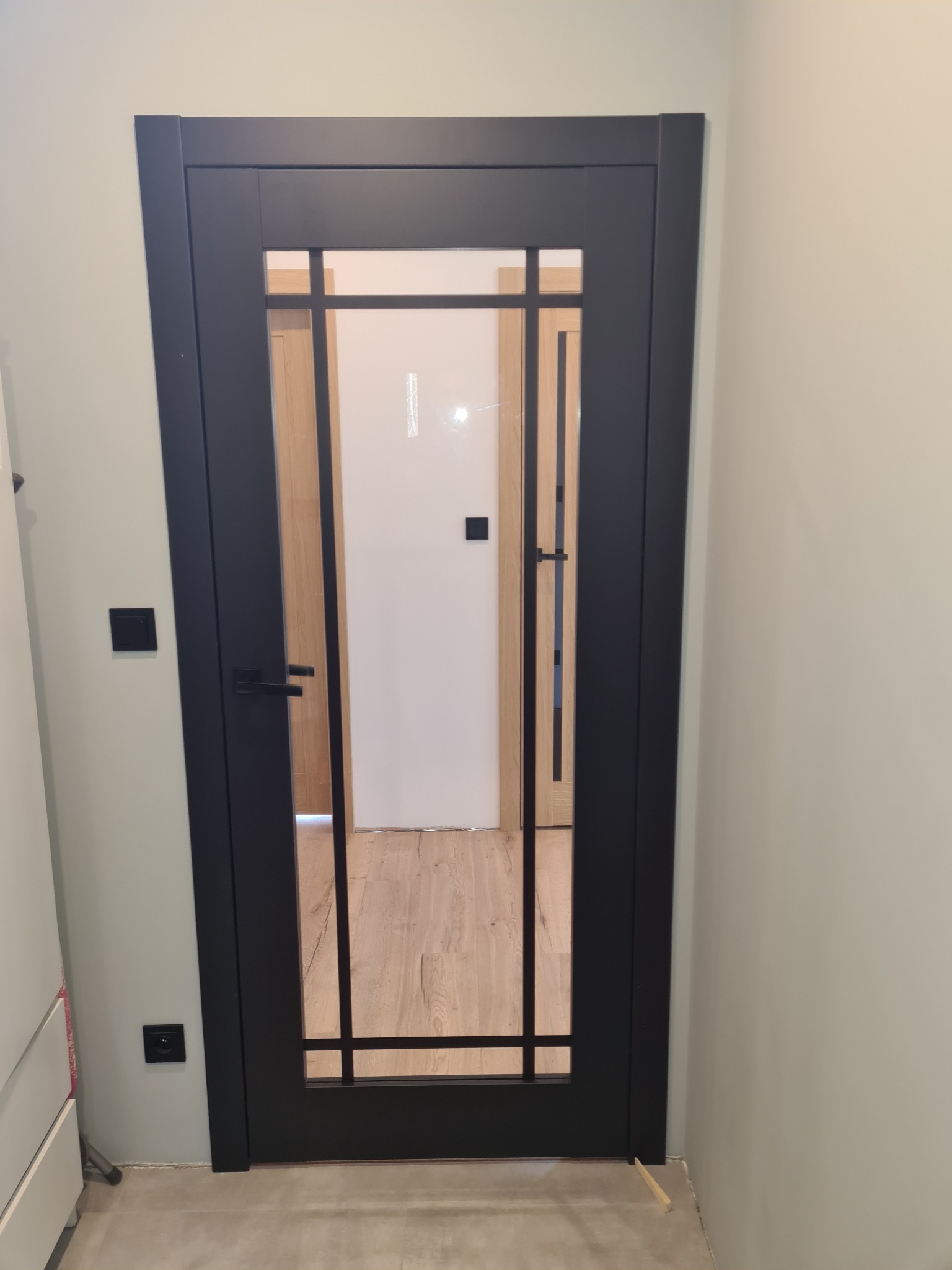 Czarne, przeszklone drzwi wewnętrzne z klamką, zamontowane w mieszkaniu w Rudzie Śląskiej. Widoczny fragment podłogi i ściany.