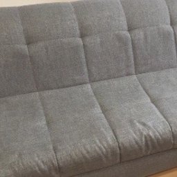 Czysto Pranie - Szara, tekstylna kanapa z wyraźnymi, kwadratowymi przeszyciami, widoczna z bliska, z lekkimi śladami użytkowania.