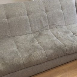 Czysto Pranie - Szara, modułowa kanapa z widocznymi, ciemniejszymi plamami na oparciu i siedzisku, sugerującymi zabrudzenia przed czyszczeniem.