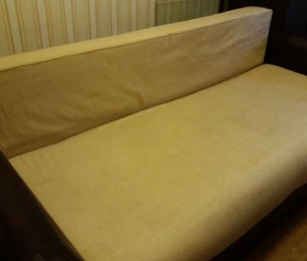 Beżowa kanapa z widocznym, okrągłym śladem po plamie na siedzisku, ukazana w lekko przytłumionym świetle domowym.