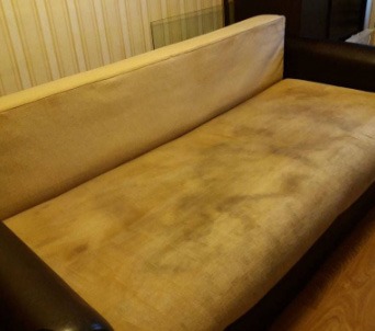 Beżowa kanapa z widocznymi, ciemnymi plamami i zabrudzeniami na siedzisku, ukazująca potrzebę czyszczenia tapicerki.