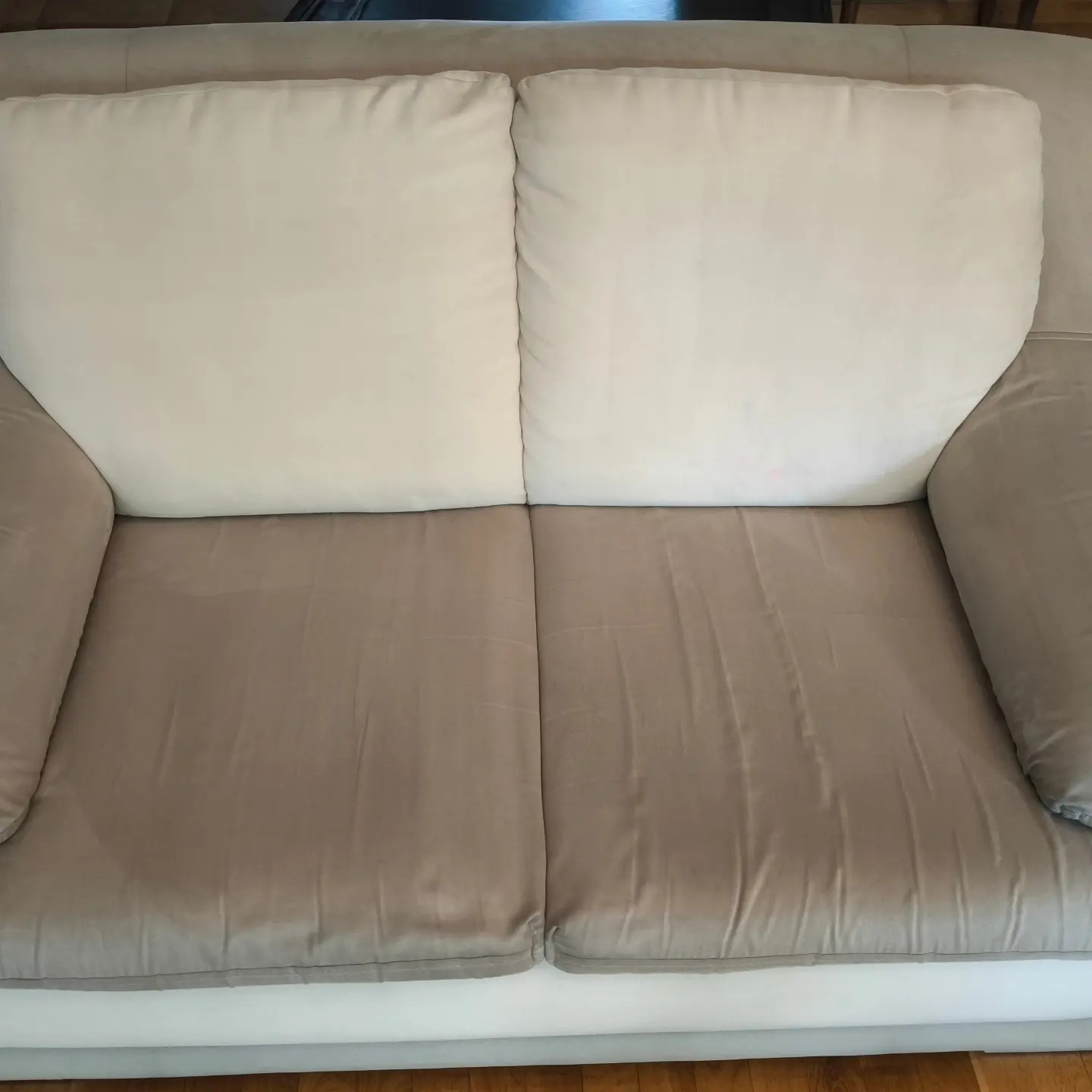 Dwuosobowa kanapa z jasnymi poduszkami po lewej stronie wyraźnie czystsza po zabiegu czyszczenia tapicerki niż po prawej stronie.