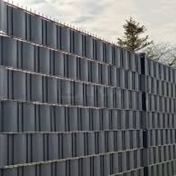 Piotr sierachan - Grafitowe panele ogrodzeniowe z tworzywa sztucznego, widoczne z bliska, z drzewem w tle. Nowoczesny design z poziomymi listwami i metalowymi słupkami.