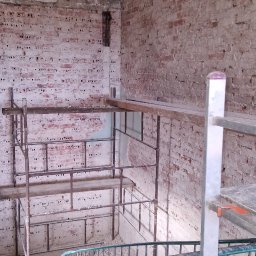 Piotr sierachan - Wnętrze budynku w trakcie rozbiórki: odsłonięta cegła, rusztowania i schody z metalową barierką. Widoczne ślady demontażu i przygotowania do dalszych prac.