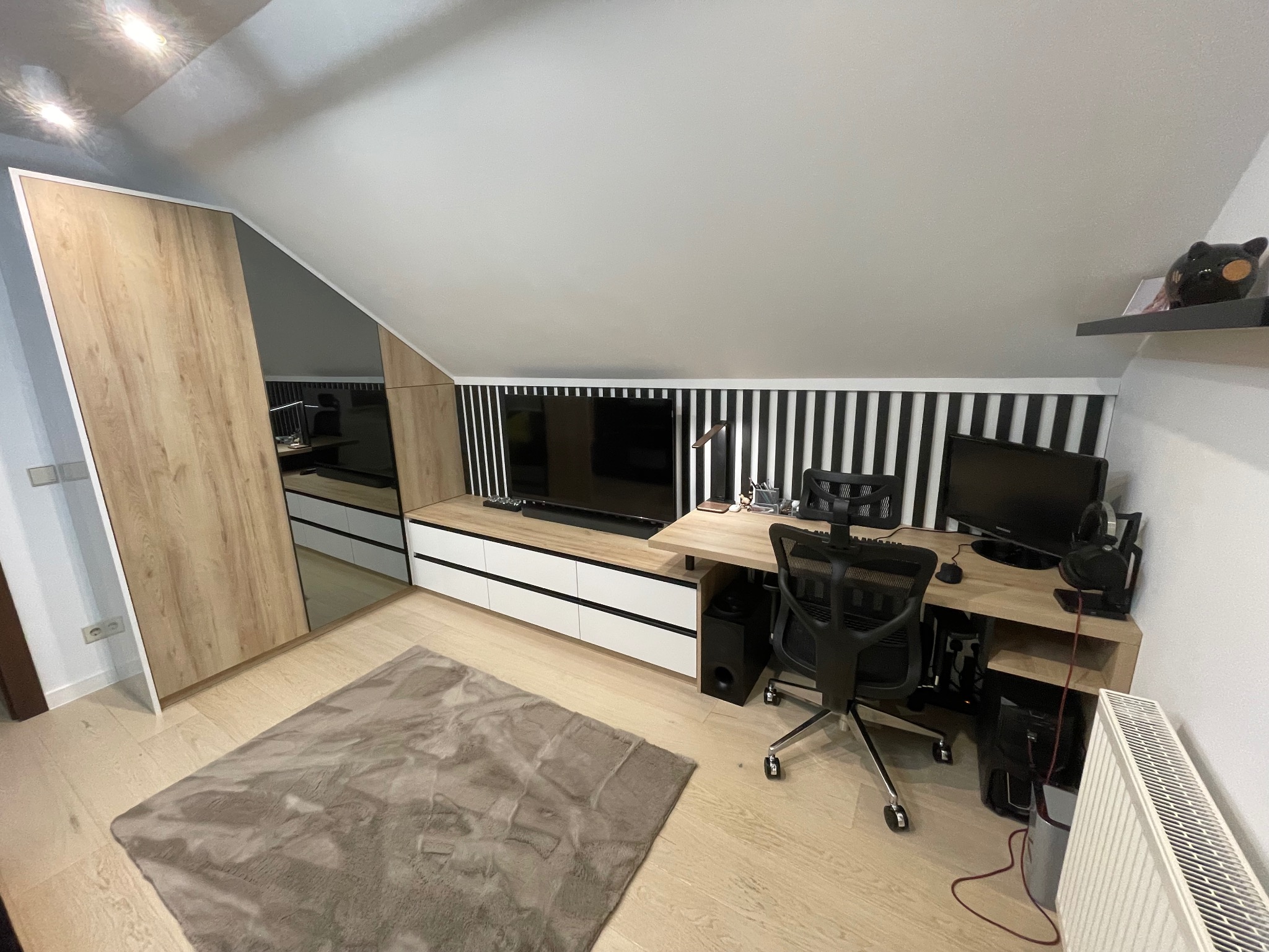 Pokój na poddaszu z szafą przesuwną z lustrem, biurkiem komputerowym i telewizorem na szafce RTV z białymi frontami.