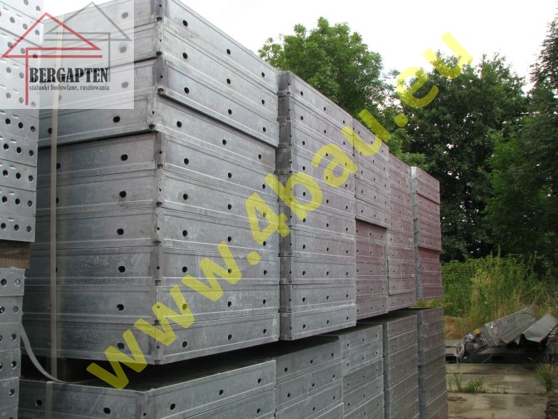 Stos szalunków ściennych Rasto, widoczne otwory montażowe i metalowa konstrukcja. Tło z zielenią drzew. Szalunki ułożone równo, gotowe do transportu.