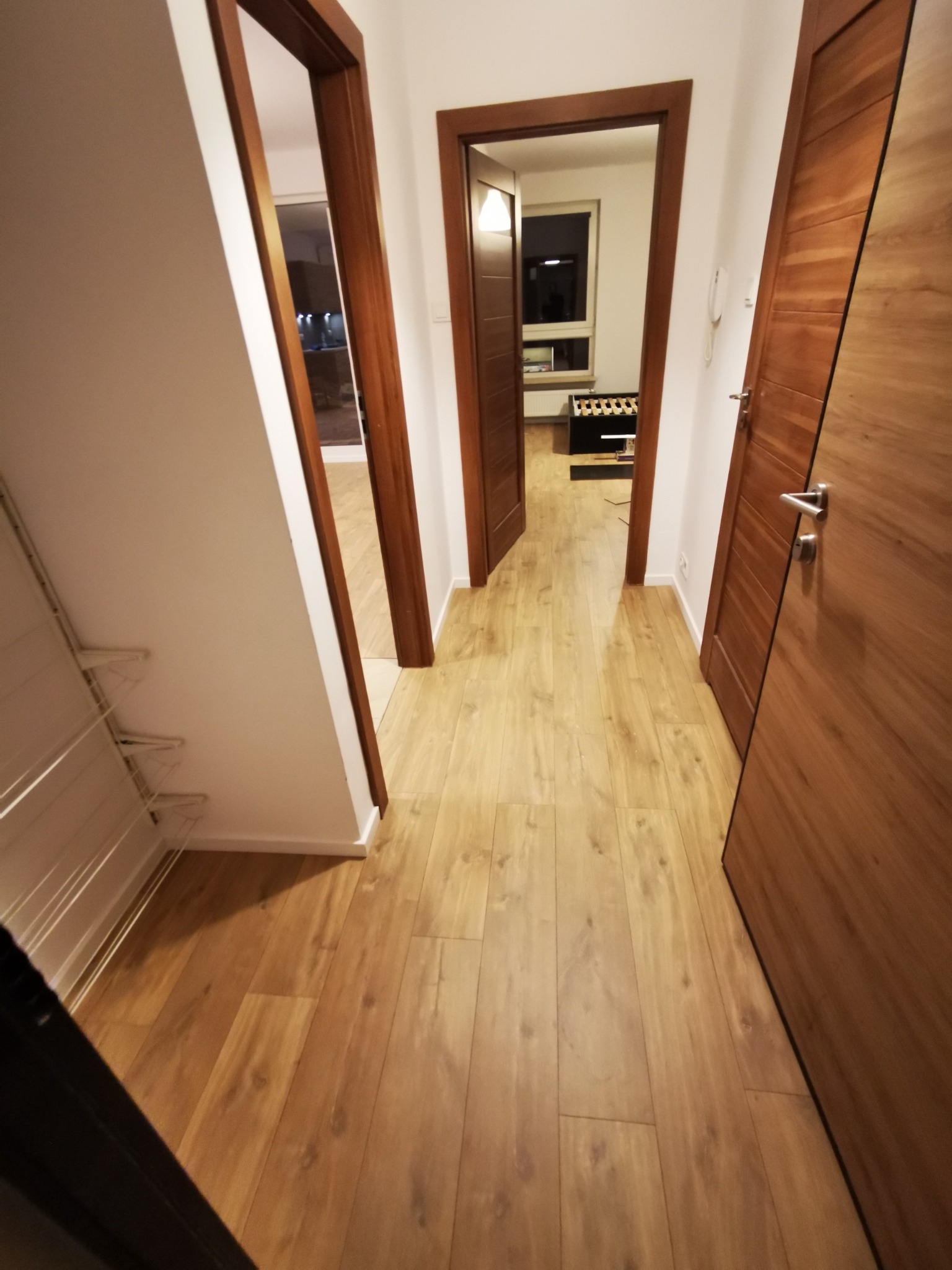 Jasne panele podłogowe ułożone w korytarzu z widocznymi trzema parami drzwi z ciemnego drewna.