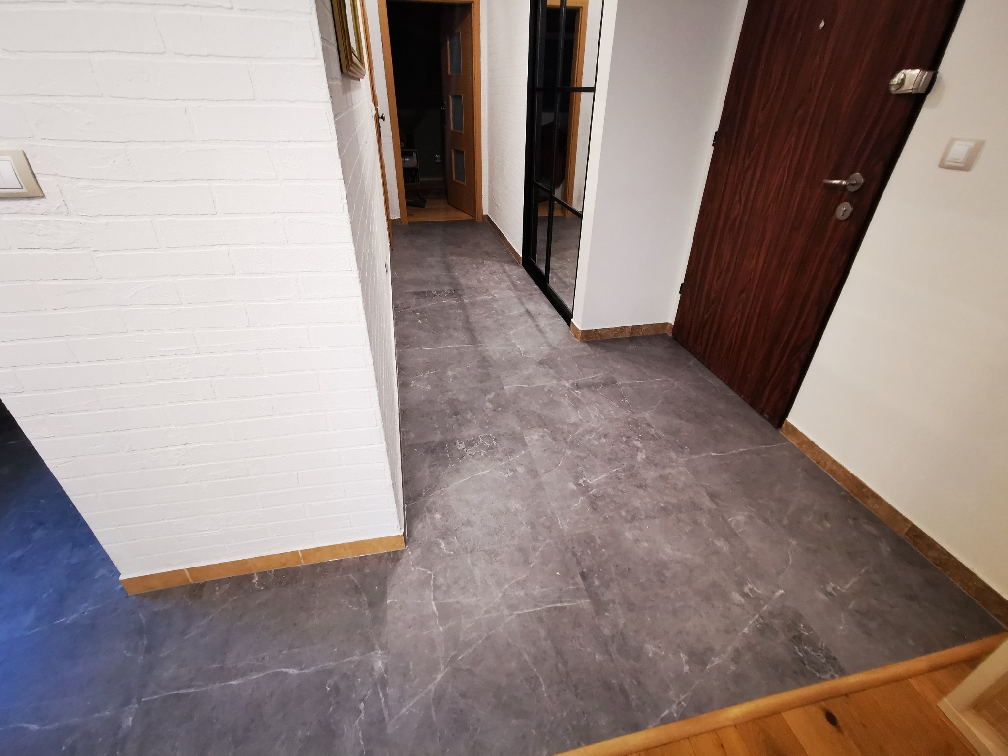 Szara podłoga z efektem marmuru w korytarzu z białymi ścianami z cegły i drewnianymi drzwiami.