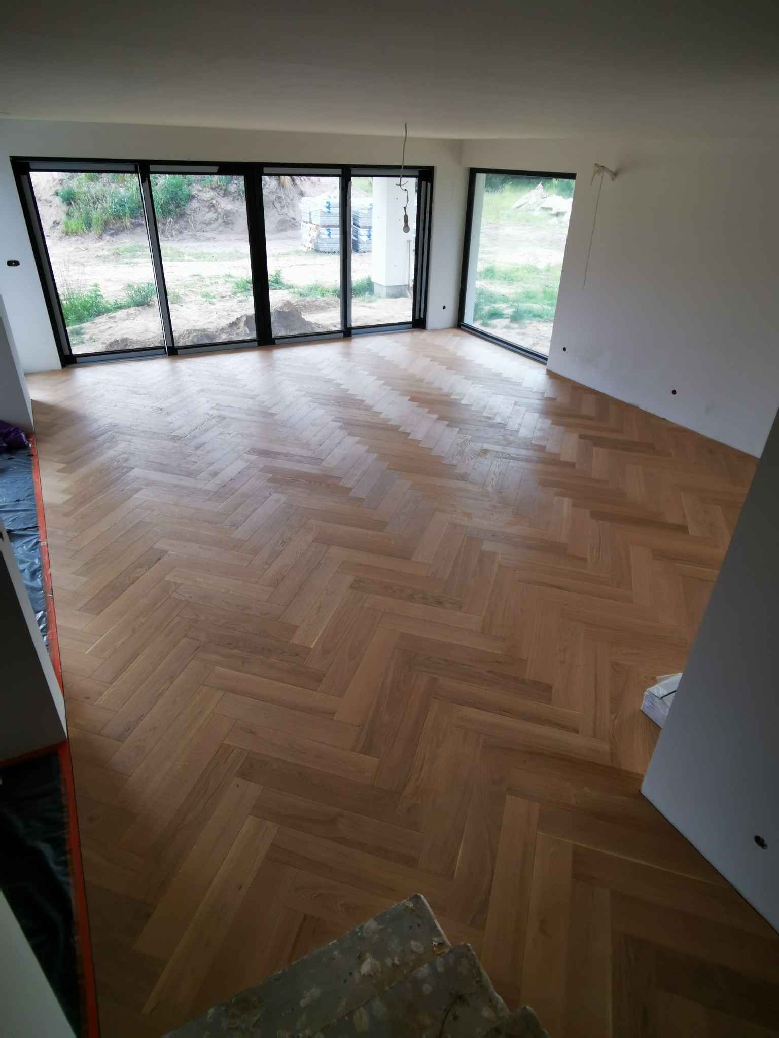 Parkiet ułożony w jodełkę francuską, w jasnym, nowoczesnym wnętrzu z dużymi oknami w Warszawie. Widoczne detale ułożenia i naturalne wybarwienie drewna.