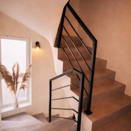 Probud Piotr Rosinski - Schody z terakoty z czarną, metalową balustradą w jasnym wnętrzu. Na parapecie wazon z suszonymi trawami. Minimalistyczny design.
