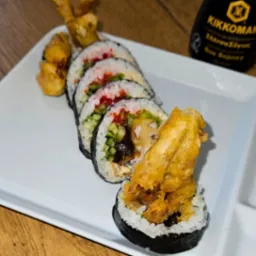 Sushi z tempurą i warzywami na białym talerzu, butelka sosu sojowego Kikkoman w tle.