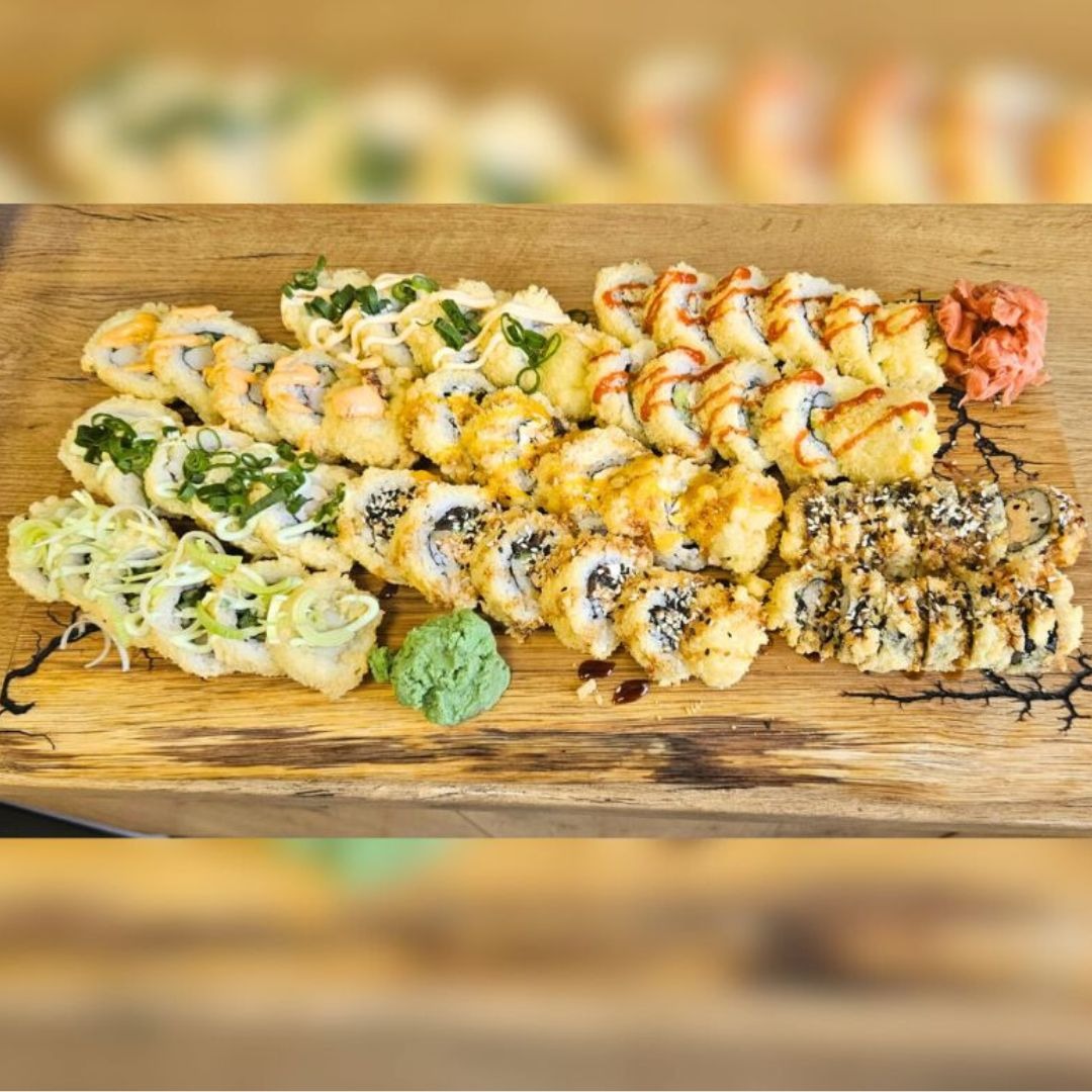 Różnorodny zestaw sushi tempura ułożony na drewnianej desce, z wasabi i imbirem, widoczne sosy i posypki.