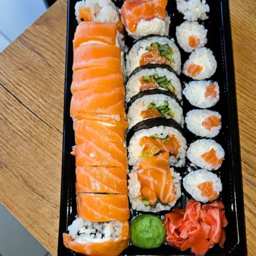 Zestaw sushi z łososiem, ogórkiem, wasabi i imbirem na czarnej tacy, ułożony na drewnianym stole.