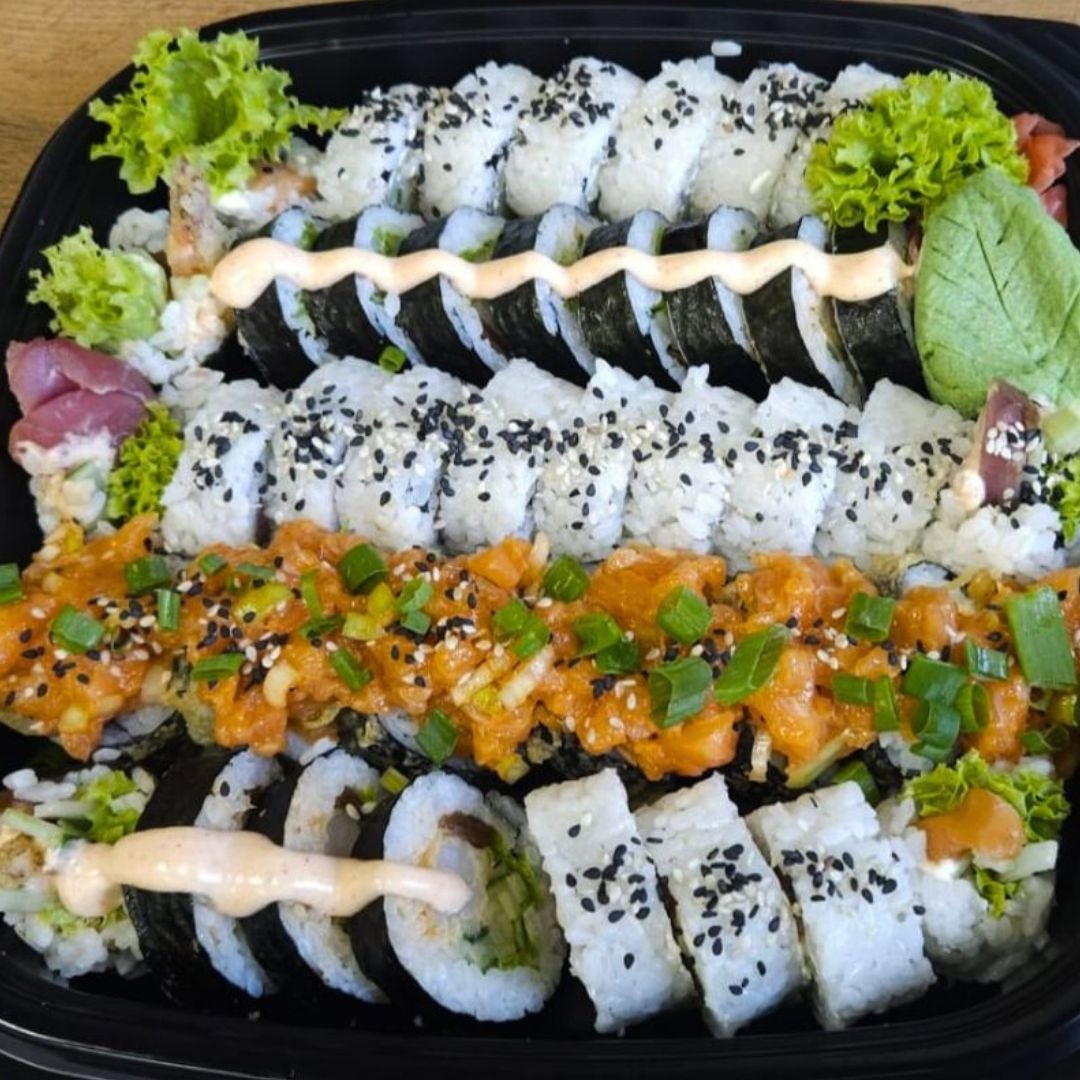 Czarny, prostokątny talerz z różnorodnym zestawem sushi: rolki z ryżem, nori, łososiem, warzywami, posypane sezamem i udekorowane sałatą.