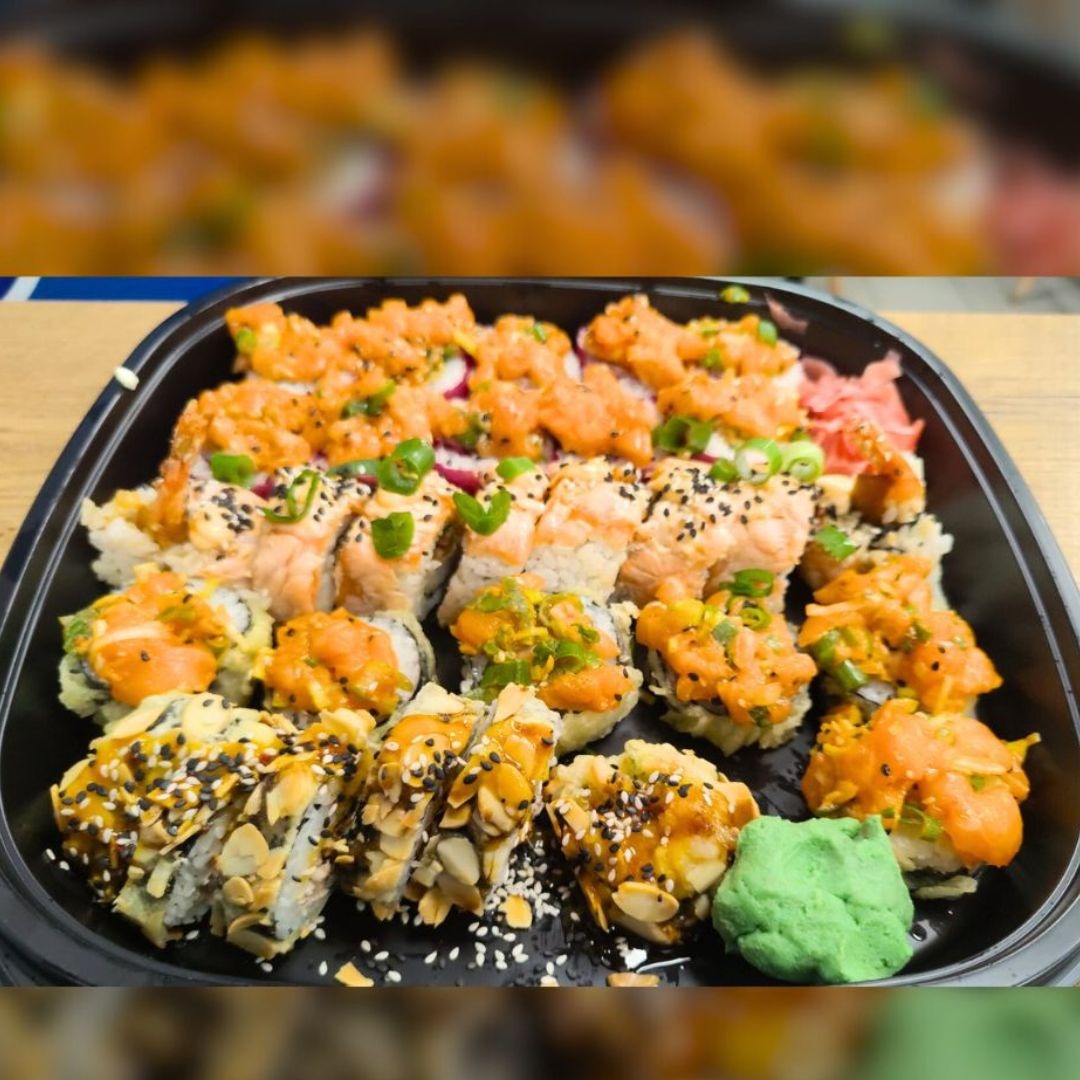 Zestaw różnorodnych rolek sushi w czarnym, plastikowym pojemniku: rolki z łososiem posypane czarnym sezamem, rolki z tempurą i migdałami, rolki z pikantnym sosem pomarańczowym, wasabi i marynowany...