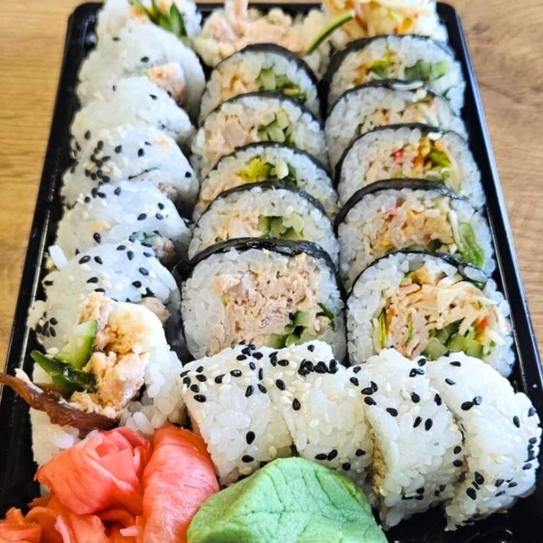 Zestaw sushi z różnymi rodzajami rolek, w tym z tuńczykiem i warzywami, podany na czarnej tacy z imbirem i wasabi.