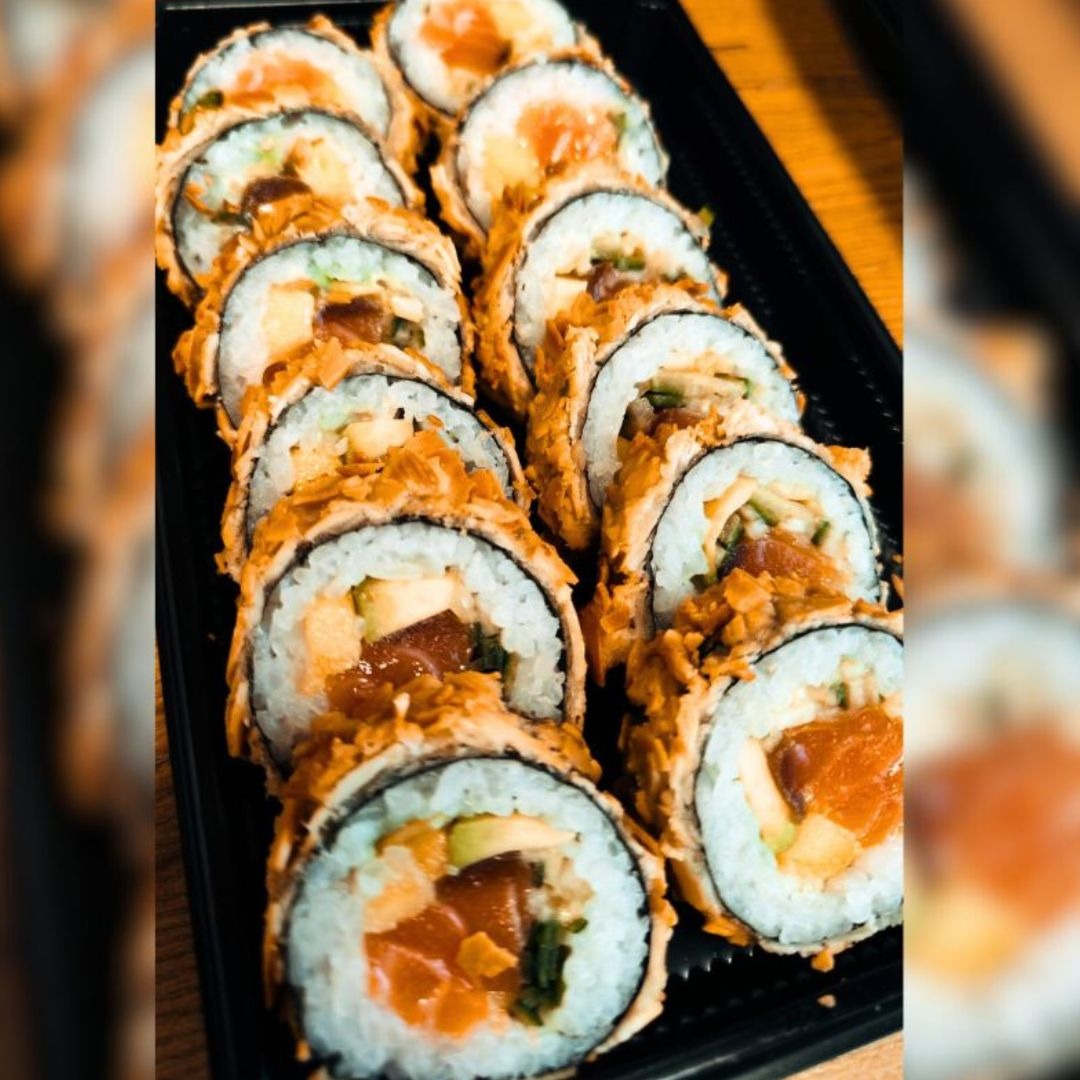 Rząd smażonych rolek sushi z łososiem, awokado i ogórkiem, ułożonych na czarnej tacy.