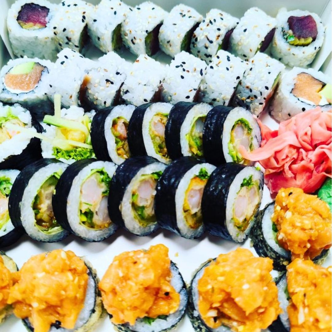 Różnorodny zestaw sushi w pudełku: rolki z tuńczykiem, łososiem, krewetkami w tempurze i pikantnym sosem, ozdobione imbirem.
