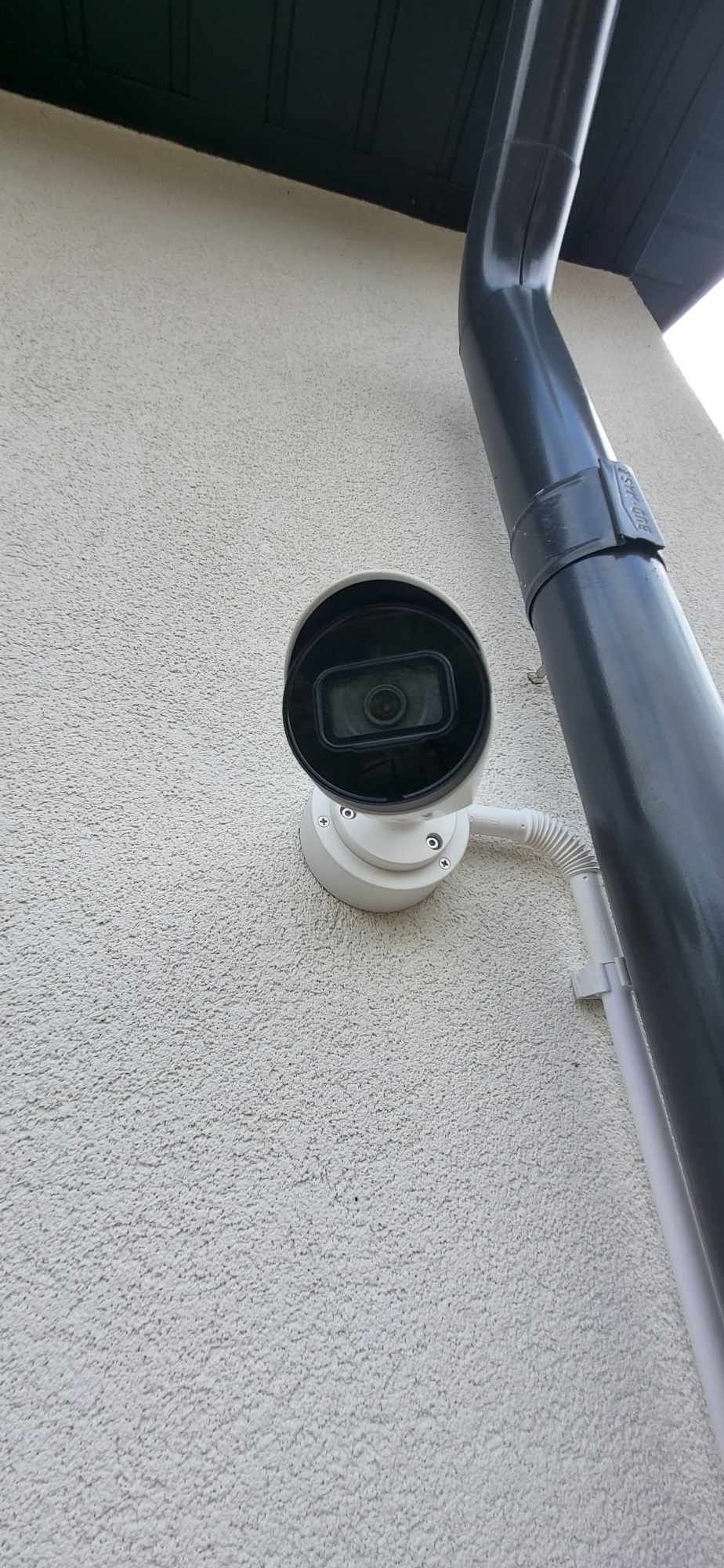Kamera monitoringu zewnętrznego, zamontowana na elewacji budynku obok rury spustowej, widok z dołu.