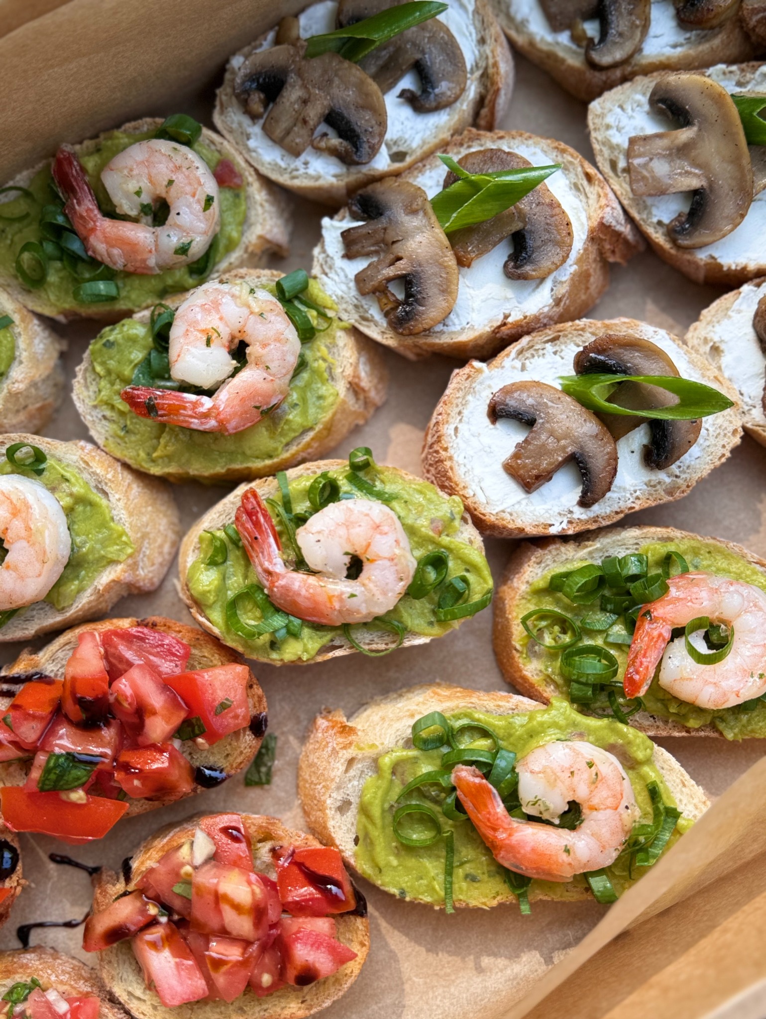 Zbliżenie na różnorodne kanapki: grzanki z awokado i krewetkami posypane szczypiorkiem, grzanki z kremowym serem i pieczarkami oraz grzanki z pomidorami skropione octem balsamicznym, ułożone...