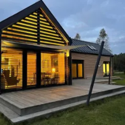 Nowoczesny dom z dużym tarasem i przeszkleniami z żaluzjami, widok z zewnątrz o zmierzchu.