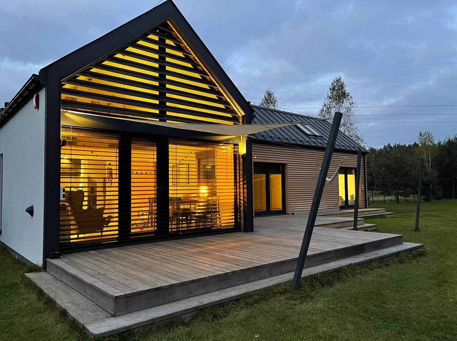 Nowoczesny dom z dużym tarasem i przeszkleniami z żaluzjami, widok z zewnątrz o zmierzchu.