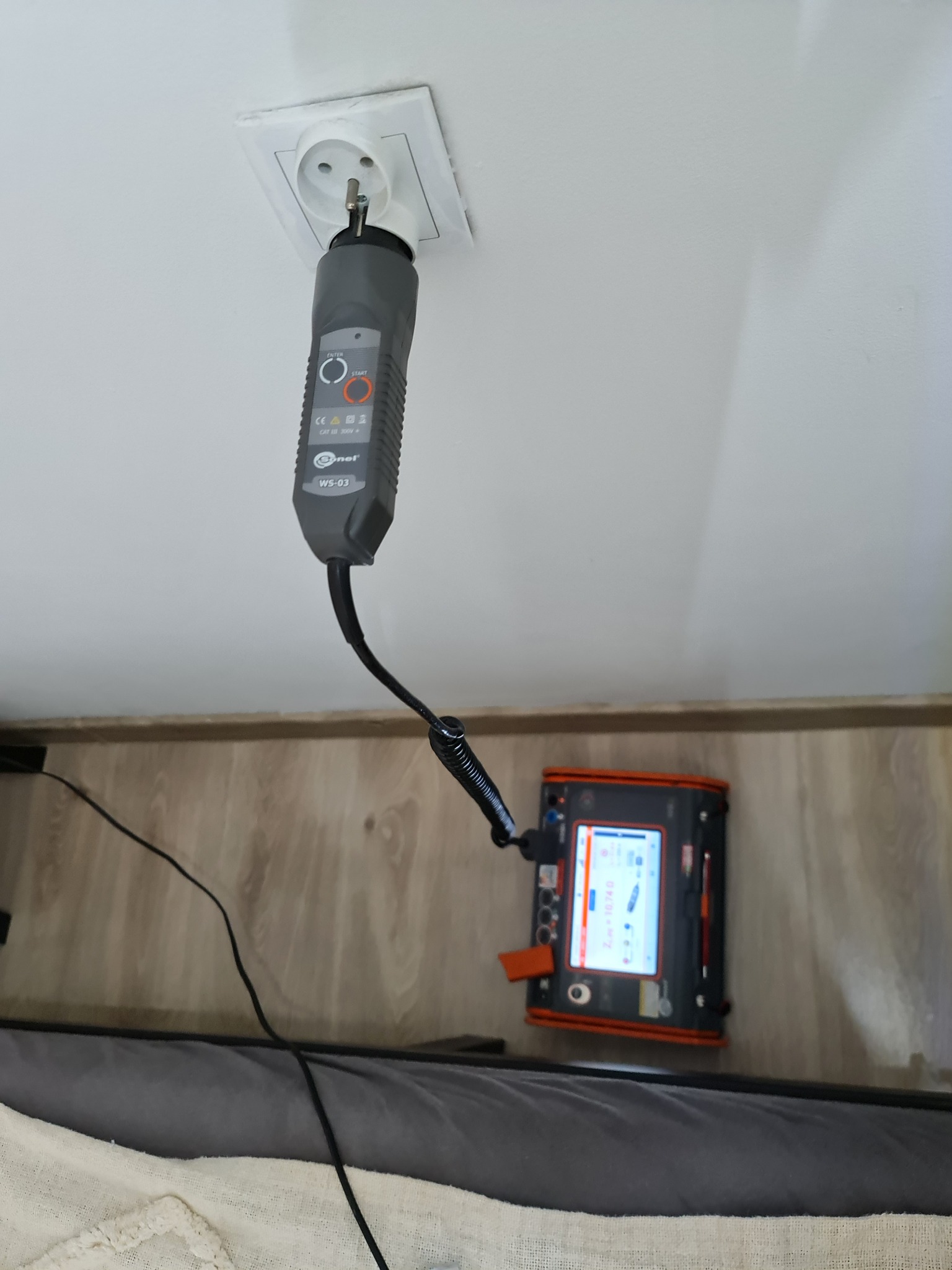 Miernik Sonel WS-03 w gniazdku elektrycznym podczas pomiarów. Widoczny ekran urządzenia z wynikami. Sprzęt do pomiarów elektrycznych w trakcie pracy.