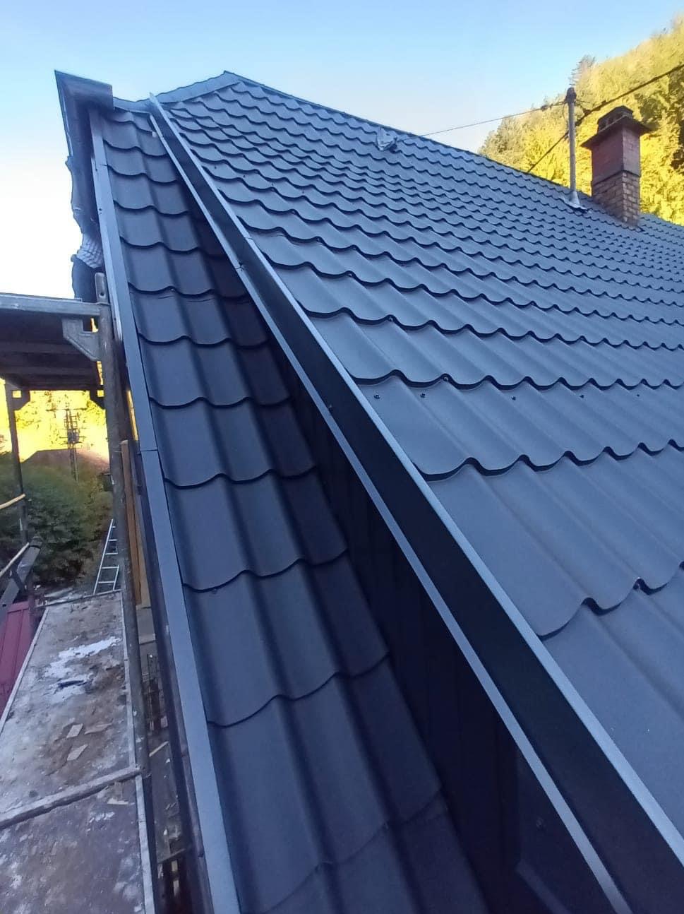 Nowy, czarny dach z blachodachówki z zamontowaną rynną w Katowicach, widoczny komin w tle.