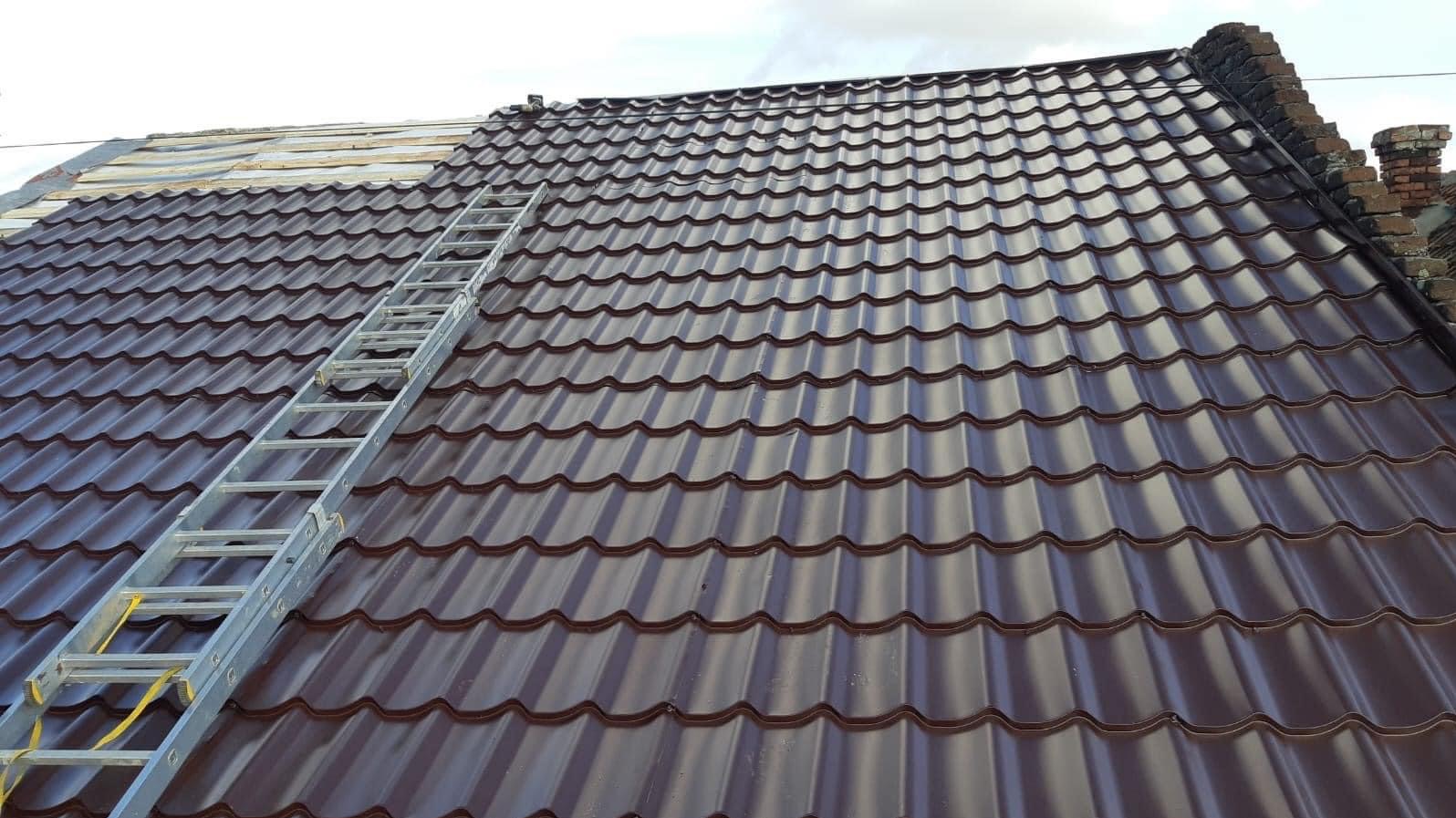 Brązowe dachówki na połowie dachu, druga połowa w trakcie prac, widoczna drabina oparta o dach.
