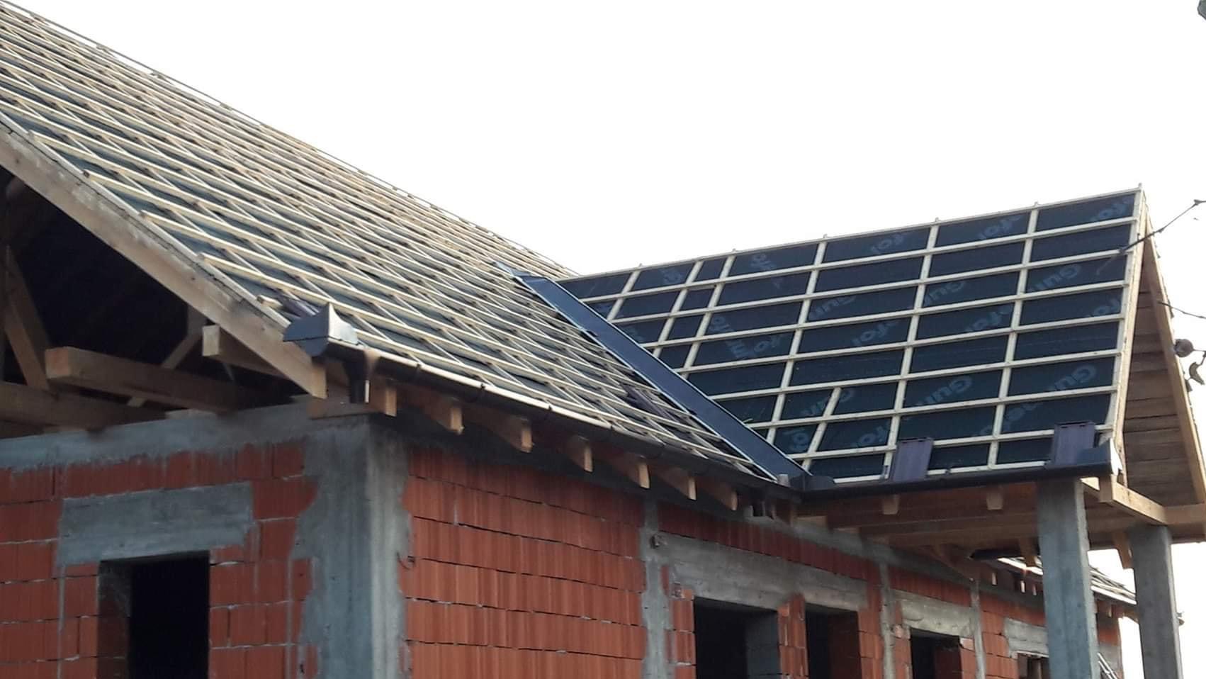 Budowa dachu domu jednorodzinnego w trakcie realizacji: widoczne więźba dachowa, membrana dachowa z łatami oraz częściowo zamontowane rynny.