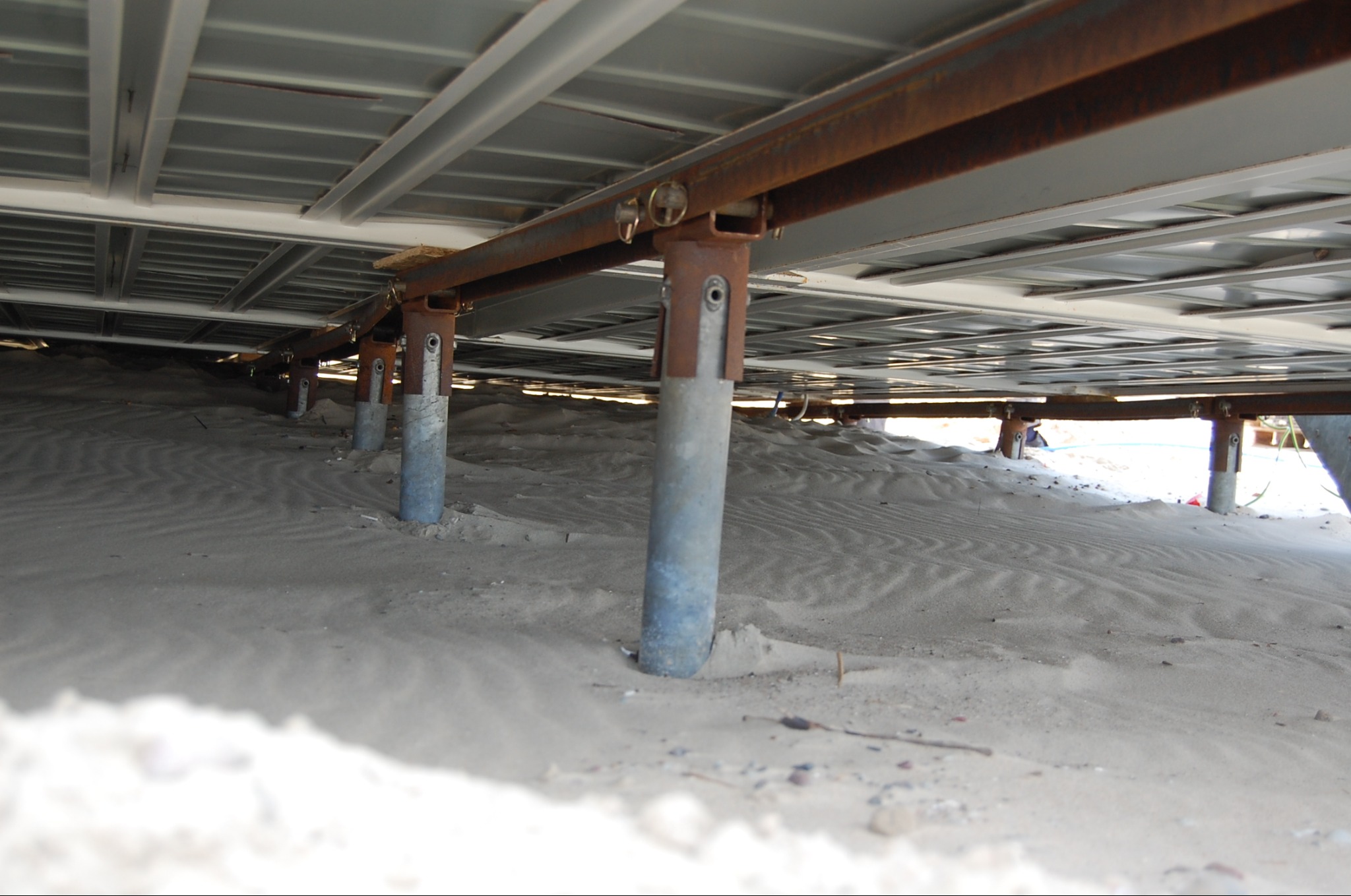 Fundamenty domu na piaszczystym podłożu, widok z dołu. Metalowe podpory i konstrukcja nośna. Nietypowe ujęcie fundamentów na piasku.